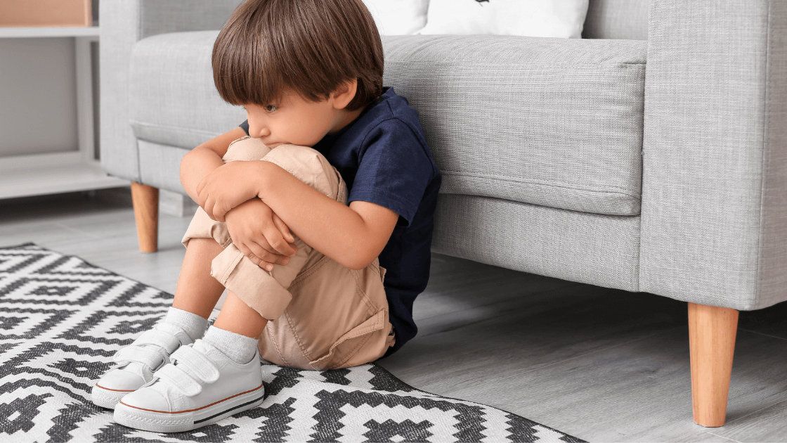 Young child sitting on floor with hands around knees, indicating digestive discomfort.