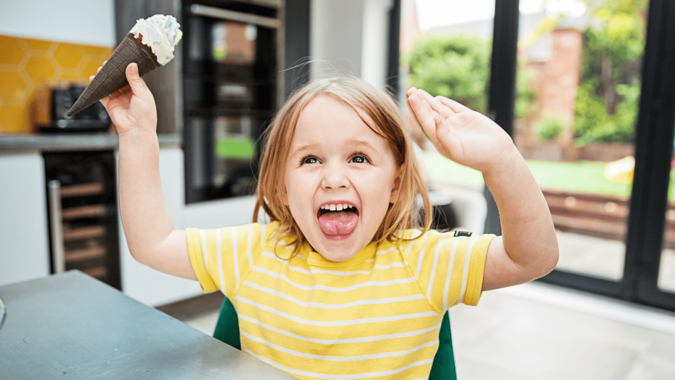 A happy child in a yellow striped shirt holding an ice cream cone